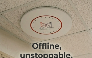 Ceiling-mounted MiSolutions vape detection device installed in a school hallway, with lockers and a wall clock visible below, highlighting offline safety monitoring.